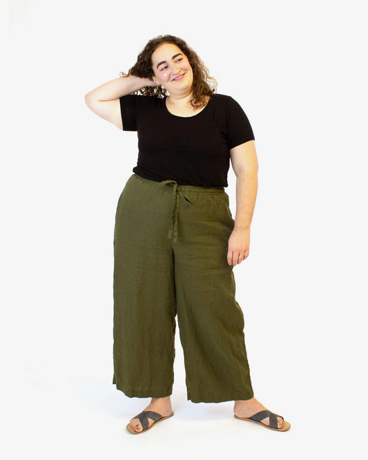 Woman wearing a black top and green wide-leg pants on a white background