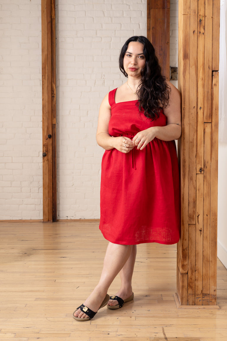 Woman in a red dress standing in a room with wooden floors and white brick walls.