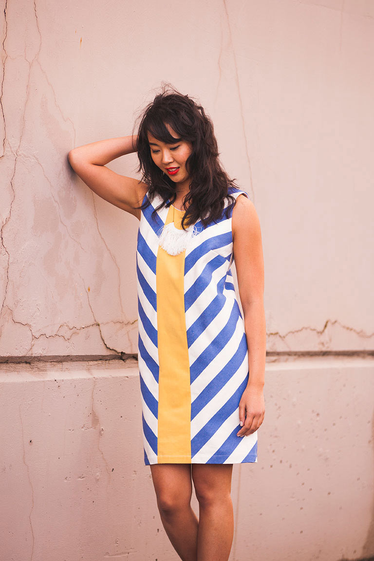 Woman wearing a blue and white striped dress with a yellow accent against a beige wall.