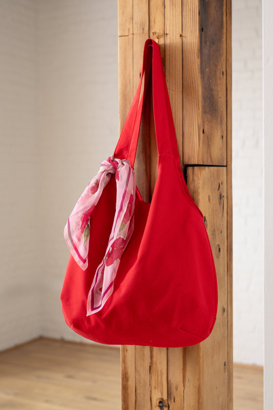Red bag with a pink scarf draped over it, hanging on a wooden door.
