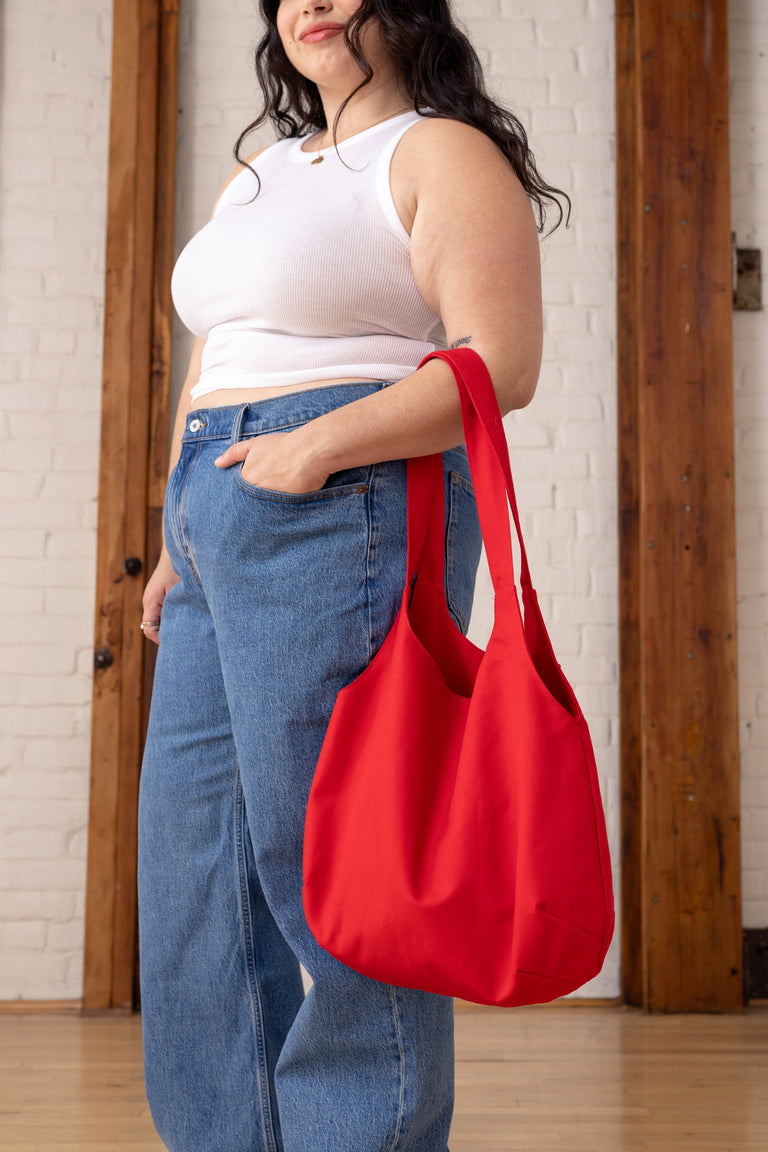 Person holding a red bag in front of a white brick wall.