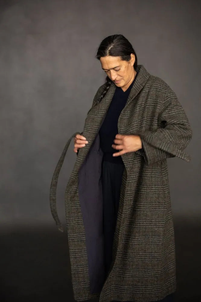 Person wearing a long dark coat against a gray background