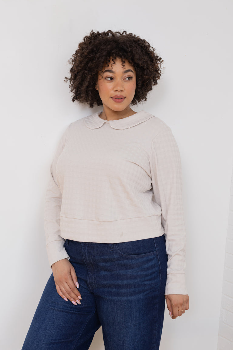 Woman wearing a beige sweater and blue jeans against a white background