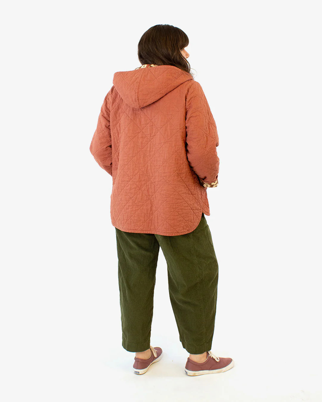 A person wearing a brown Wildwood jacket with a hood, paired with green pants and brown shoes.